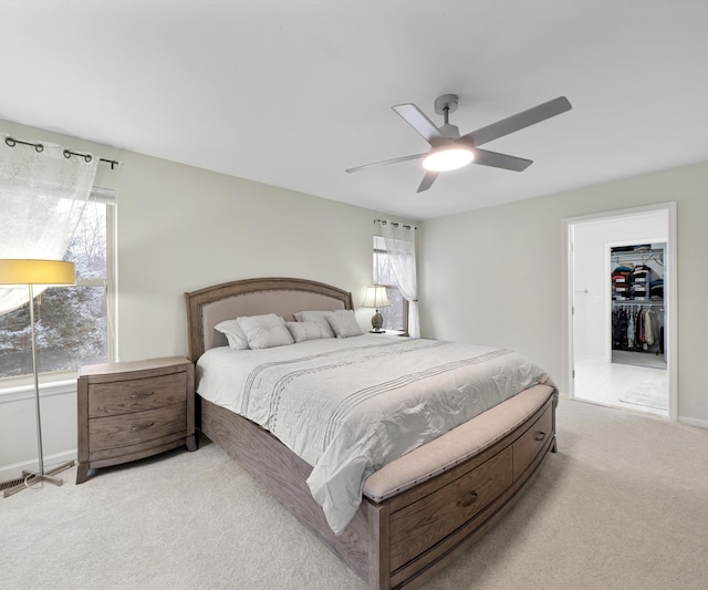 bedroom with multiple windows, a spacious closet, light carpet, and ceiling fan