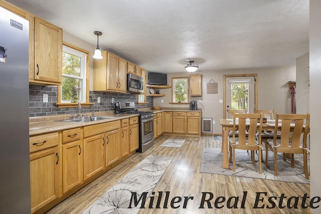 kitchen with tasteful backsplash, appliances with stainless steel finishes, decorative light fixtures, and light hardwood / wood-style floors