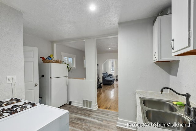 kitchen featuring sink, white cabinets, white refrigerator, light hardwood / wood-style floors, and a textured ceiling