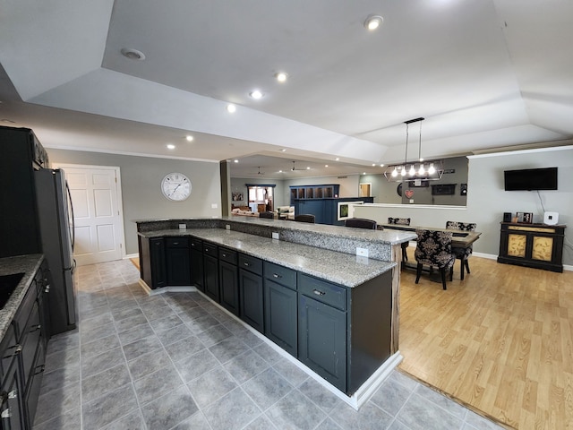 kitchen featuring a tray ceiling, decorative light fixtures, light stone counters, and stainless steel refrigerator