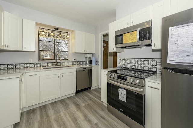 kitchen with sink, white cabinetry, stainless steel appliances, decorative backsplash, and light wood-type flooring