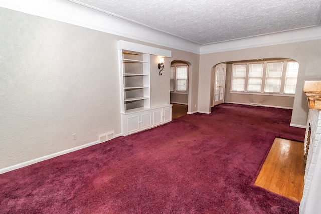 unfurnished living room with built in shelves, crown molding, a textured ceiling, and dark colored carpet