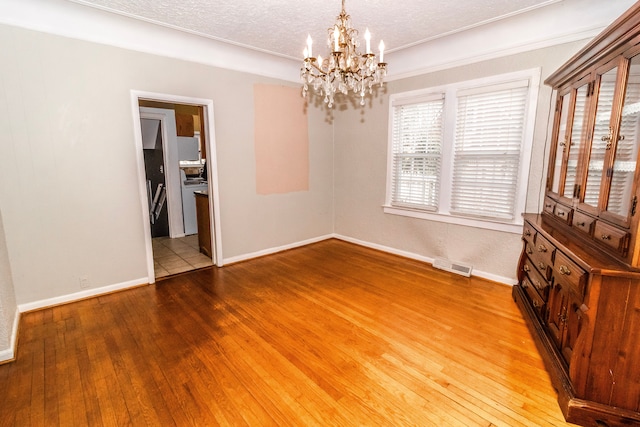 unfurnished dining area with a notable chandelier, a textured ceiling, and light hardwood / wood-style flooring