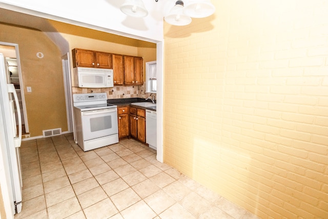 kitchen featuring light tile patterned flooring, white appliances, brick wall, and sink