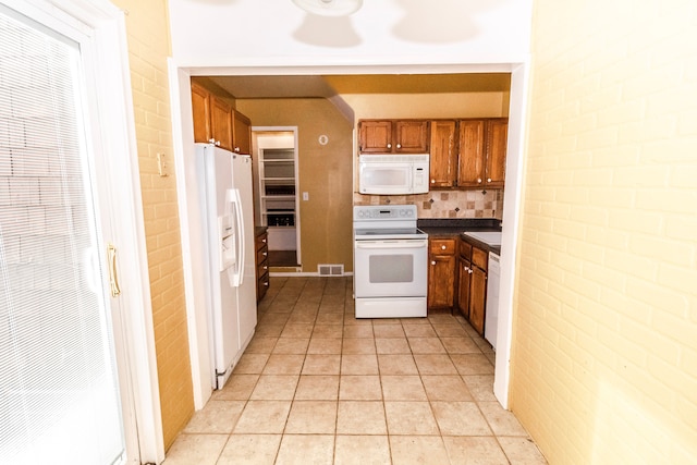 kitchen featuring light tile patterned flooring, brick wall, white appliances, and decorative backsplash