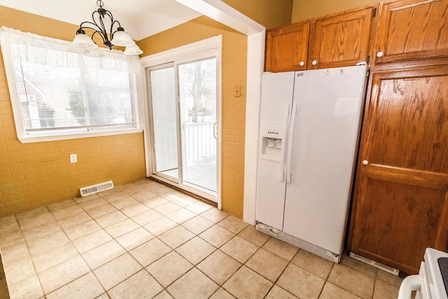 kitchen with light tile patterned floors, a notable chandelier, white refrigerator with ice dispenser, brick wall, and decorative light fixtures