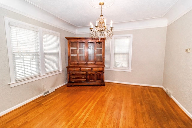 spare room with hardwood / wood-style flooring, crown molding, and a chandelier