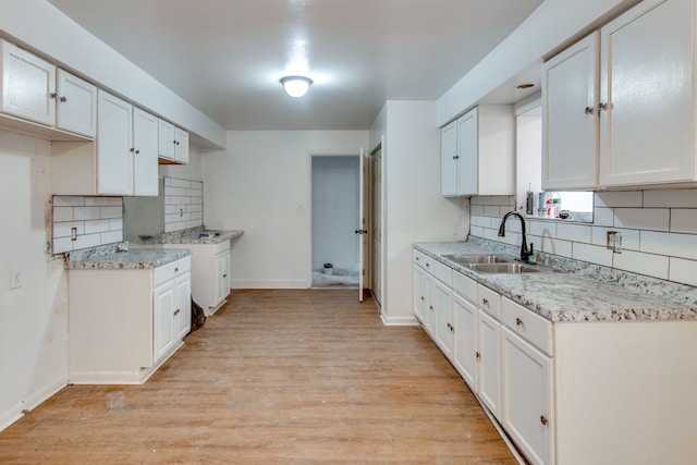 kitchen with sink, tasteful backsplash, light stone counters, light hardwood / wood-style floors, and white cabinets