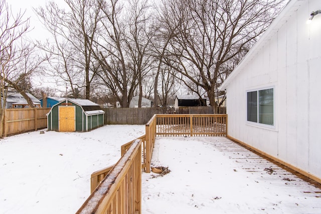 yard covered in snow with a wooden deck and a storage unit