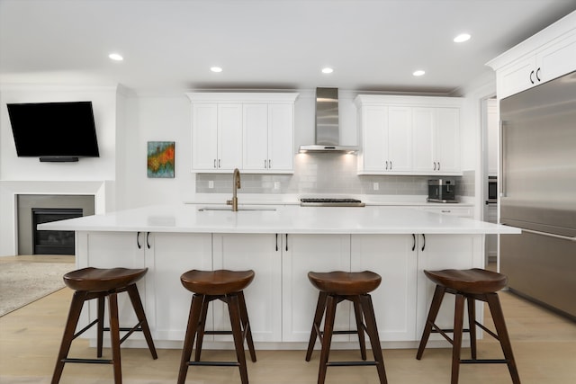 kitchen featuring built in fridge, a breakfast bar, white cabinetry, sink, and wall chimney exhaust hood