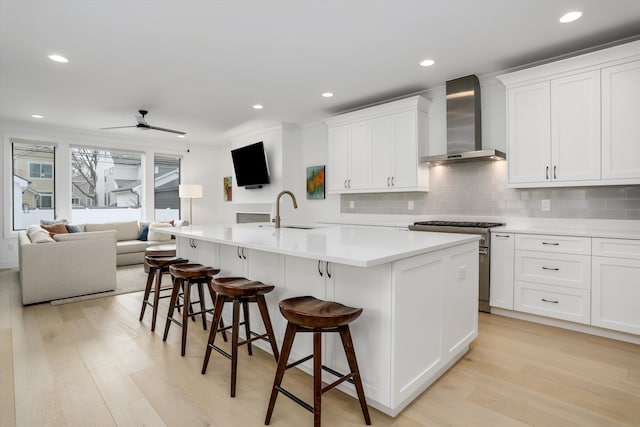 kitchen featuring an island with sink, white cabinetry, sink, high end stainless steel range oven, and wall chimney exhaust hood