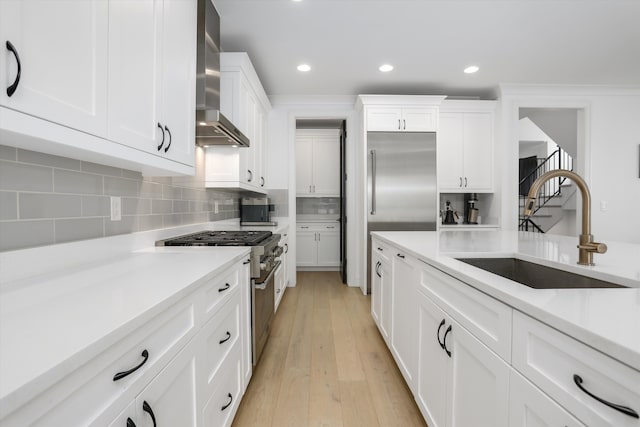 kitchen with white cabinetry, high end appliances, sink, and wall chimney exhaust hood