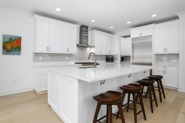 kitchen featuring built in fridge, an island with sink, white cabinetry, and wall chimney exhaust hood