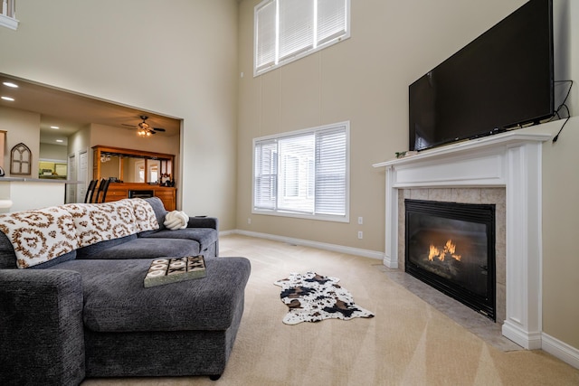 living room featuring light carpet, a tiled fireplace, ceiling fan, and a towering ceiling