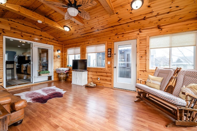 living room with wooden walls, lofted ceiling with beams, ceiling fan, wood ceiling, and light wood-type flooring