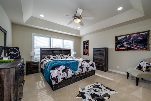 carpeted bedroom with a raised ceiling and ceiling fan