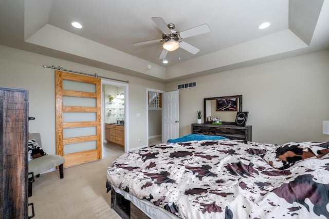 carpeted bedroom with ceiling fan, a raised ceiling, and ensuite bath