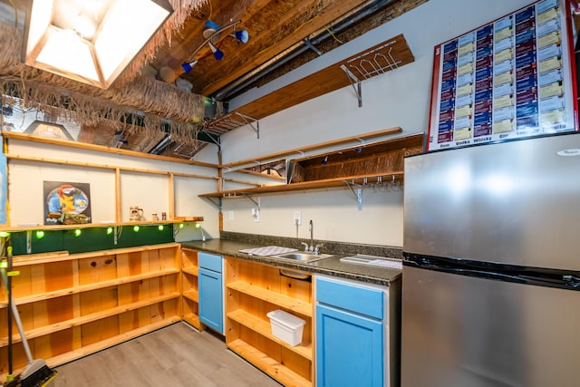 kitchen with blue cabinets, stainless steel fridge, sink, and light wood-type flooring