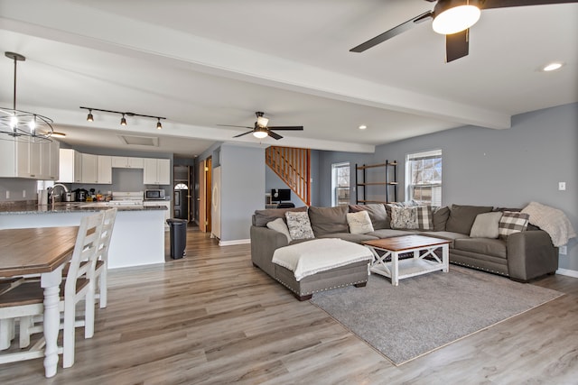 living room with ceiling fan, beam ceiling, sink, and light hardwood / wood-style flooring