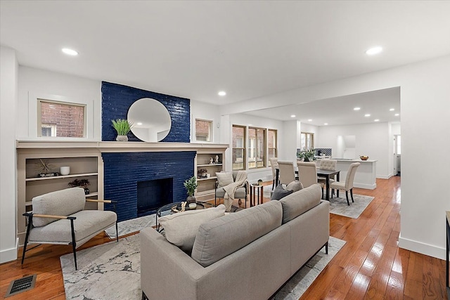 living room featuring built in features, a fireplace, and light wood-type flooring