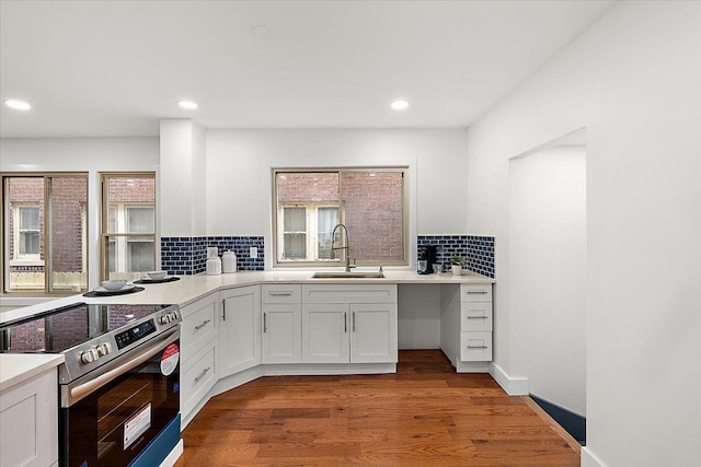 kitchen with hardwood / wood-style floors, white cabinetry, sink, stainless steel range with electric cooktop, and backsplash