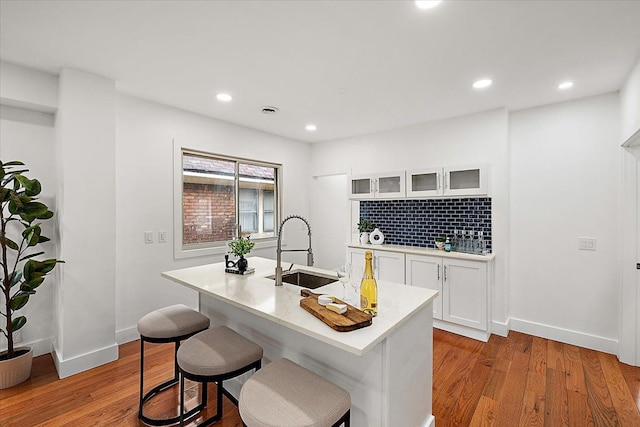 kitchen featuring hardwood / wood-style flooring, white cabinetry, a kitchen island with sink, and sink