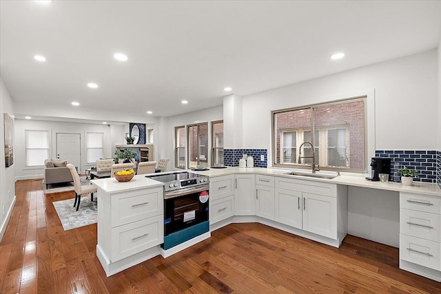 kitchen with sink, electric range, kitchen peninsula, hardwood / wood-style flooring, and white cabinets