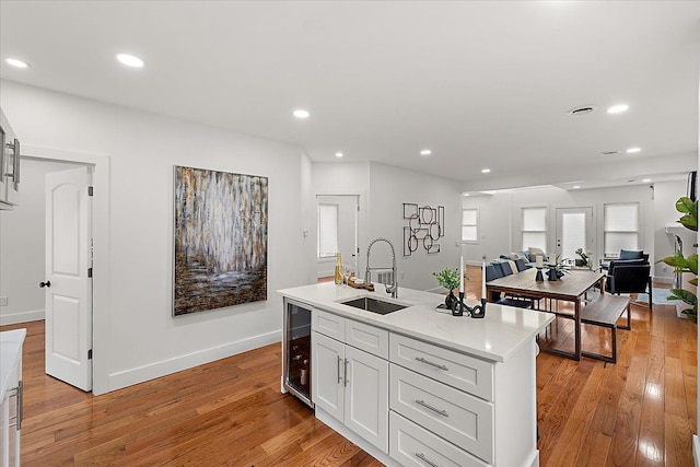 kitchen featuring sink, light hardwood / wood-style flooring, a center island with sink, beverage cooler, and white cabinets