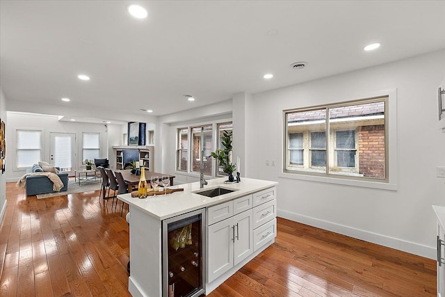 kitchen featuring white cabinetry, sink, beverage cooler, a kitchen island with sink, and light hardwood / wood-style floors