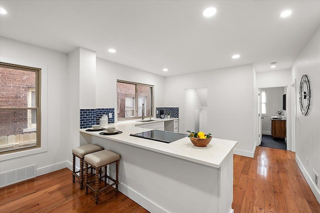 kitchen featuring sink, a kitchen bar, black electric stovetop, light hardwood / wood-style floors, and kitchen peninsula