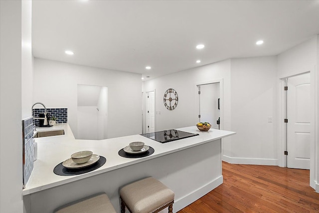 kitchen with sink, a breakfast bar area, wood-type flooring, black electric cooktop, and kitchen peninsula