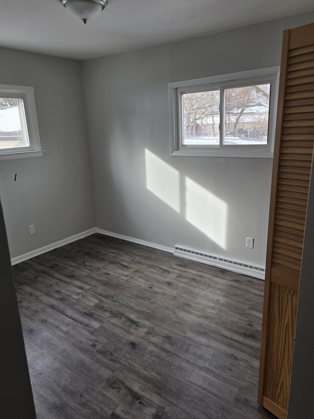 empty room featuring a baseboard heating unit and dark wood-type flooring