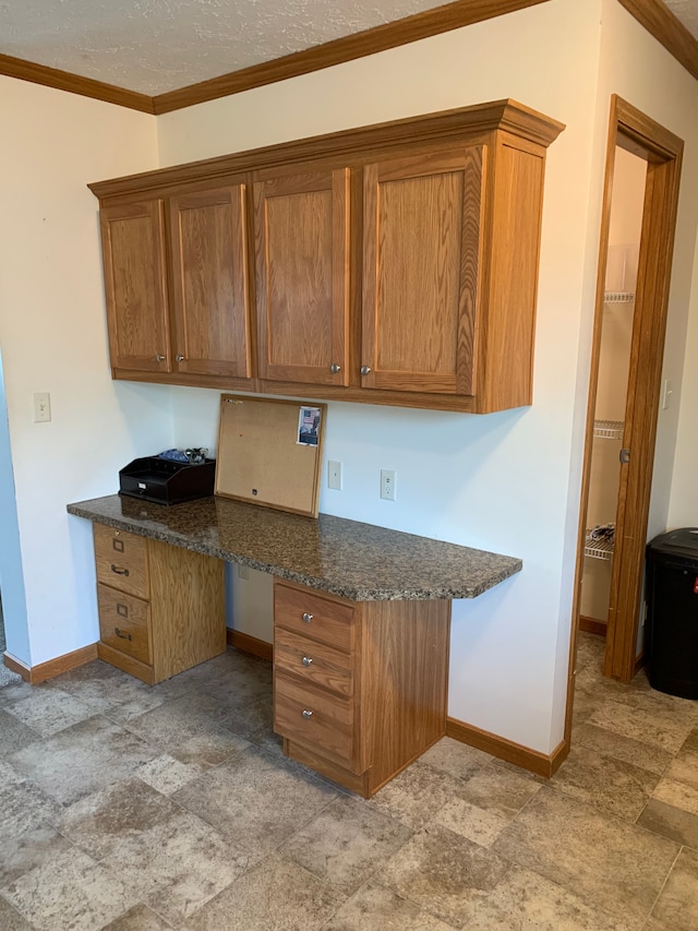 kitchen with dark stone countertops, crown molding, and built in desk