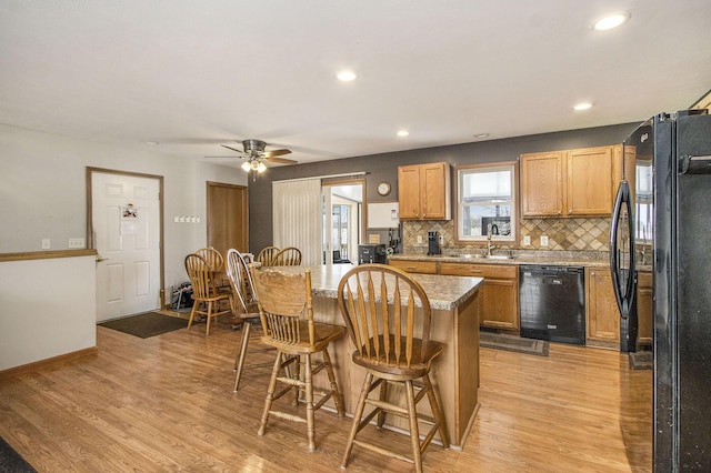 kitchen featuring light hardwood / wood-style floors, decorative backsplash, black appliances, and a kitchen breakfast bar