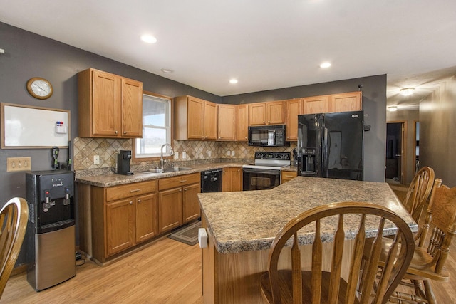 kitchen with sink, a center island, tasteful backsplash, black appliances, and light hardwood / wood-style floors