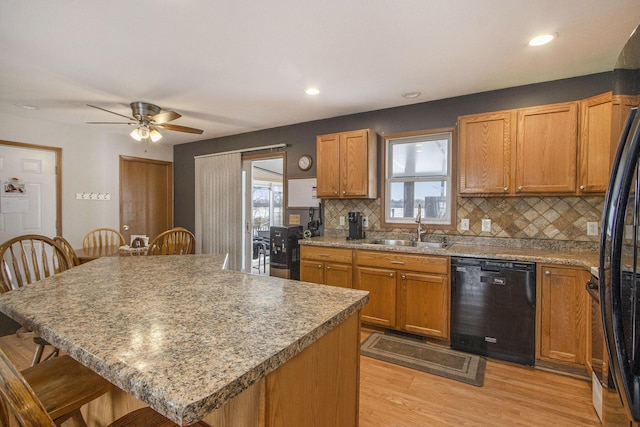 kitchen with a kitchen bar, sink, light hardwood / wood-style flooring, decorative backsplash, and black appliances