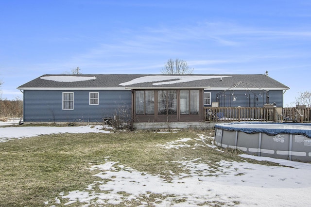 snow covered rear of property featuring a yard, a sunroom, and a covered pool