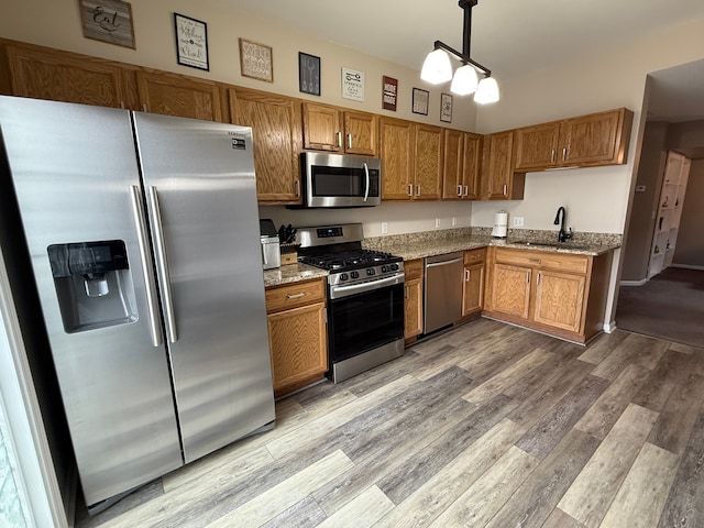 kitchen featuring pendant lighting, appliances with stainless steel finishes, light stone countertops, and sink