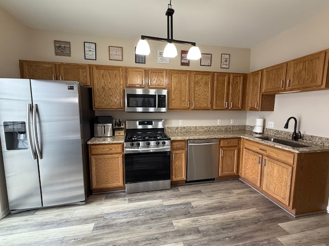 kitchen with stone counters, appliances with stainless steel finishes, pendant lighting, sink, and light hardwood / wood-style floors