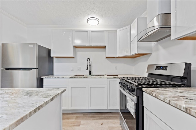 kitchen with appliances with stainless steel finishes, white cabinetry, sink, wall chimney range hood, and light hardwood / wood-style flooring