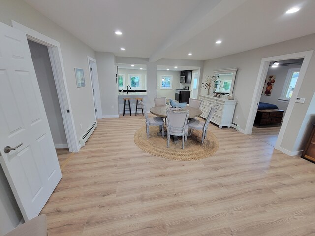 dining space featuring sink, light hardwood / wood-style floors, a healthy amount of sunlight, and baseboard heating