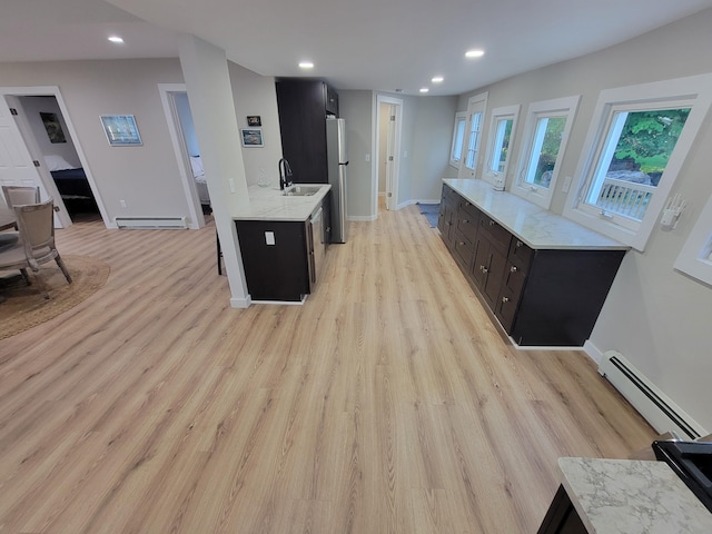 kitchen with sink, light stone counters, light hardwood / wood-style flooring, baseboard heating, and stainless steel fridge