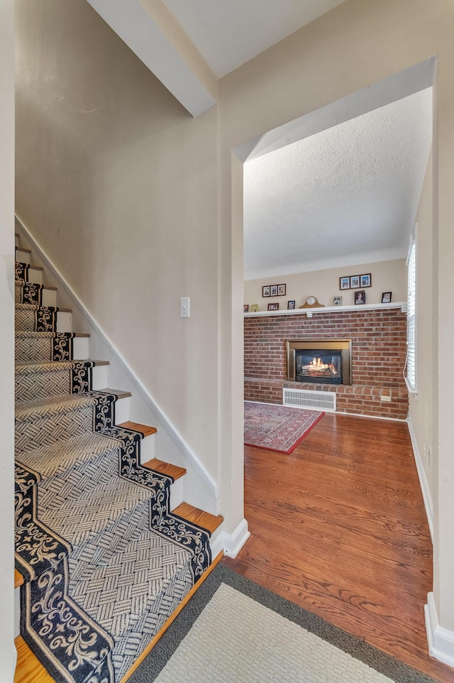 staircase with hardwood / wood-style floors, a textured ceiling, and a brick fireplace