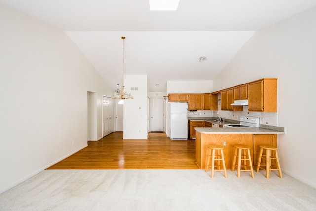 kitchen featuring white appliances, a breakfast bar area, high vaulted ceiling, kitchen peninsula, and a chandelier