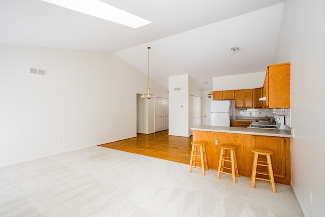 kitchen with a breakfast bar area, backsplash, lofted ceiling with skylight, kitchen peninsula, and white fridge