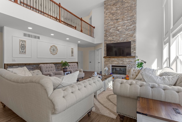 living room with hardwood / wood-style flooring, a stone fireplace, and a towering ceiling