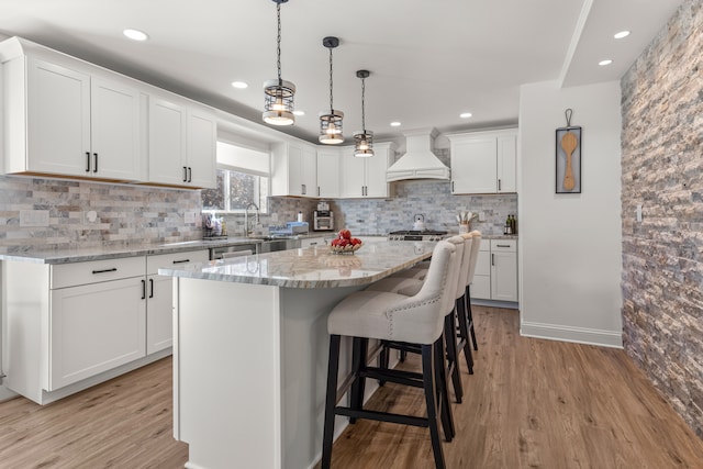 kitchen with light stone counters, custom range hood, white cabinets, and a center island