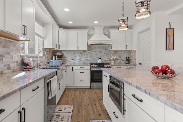 kitchen with white cabinetry, appliances with stainless steel finishes, light stone countertops, and custom exhaust hood