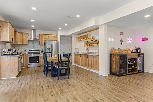 kitchen featuring backsplash, stainless steel appliances, light hardwood / wood-style floors, and wall chimney exhaust hood