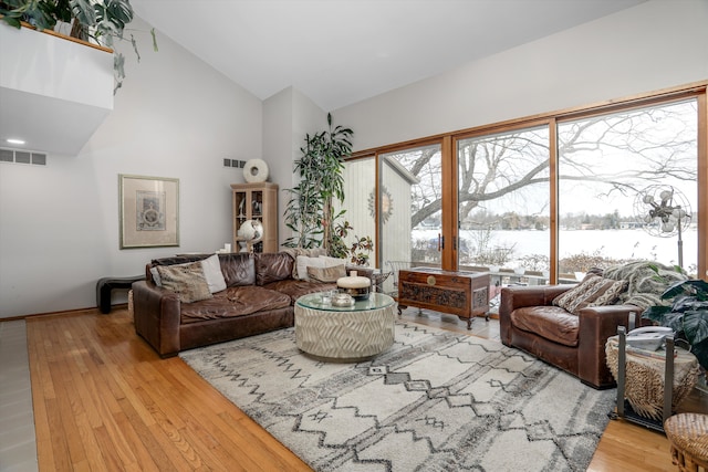 living room featuring high vaulted ceiling, a water view, and light wood-type flooring